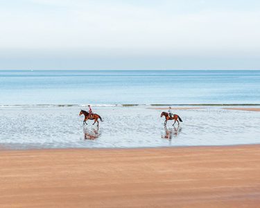 two people horseback riding on the beach