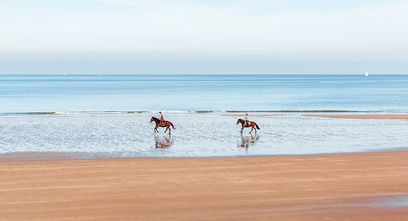 two people horseback riding on the beach