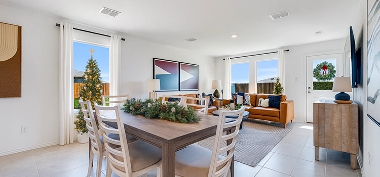 Modern open living and dining room with a holiday centerpiece and small Christmas trees by the windows.