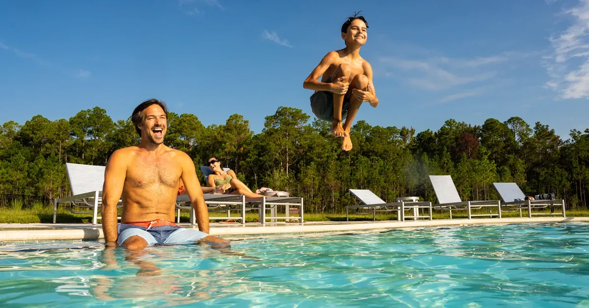 Father and son enjoy quality time at a luxury resort pool with pristine facilities and scenic forest views on a sunny day.