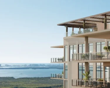 Luxury high-rise condominium balconies with glass railings and rooftop pergola overlook a stunning panoramic coastal view with turquoise waters and city skyl...